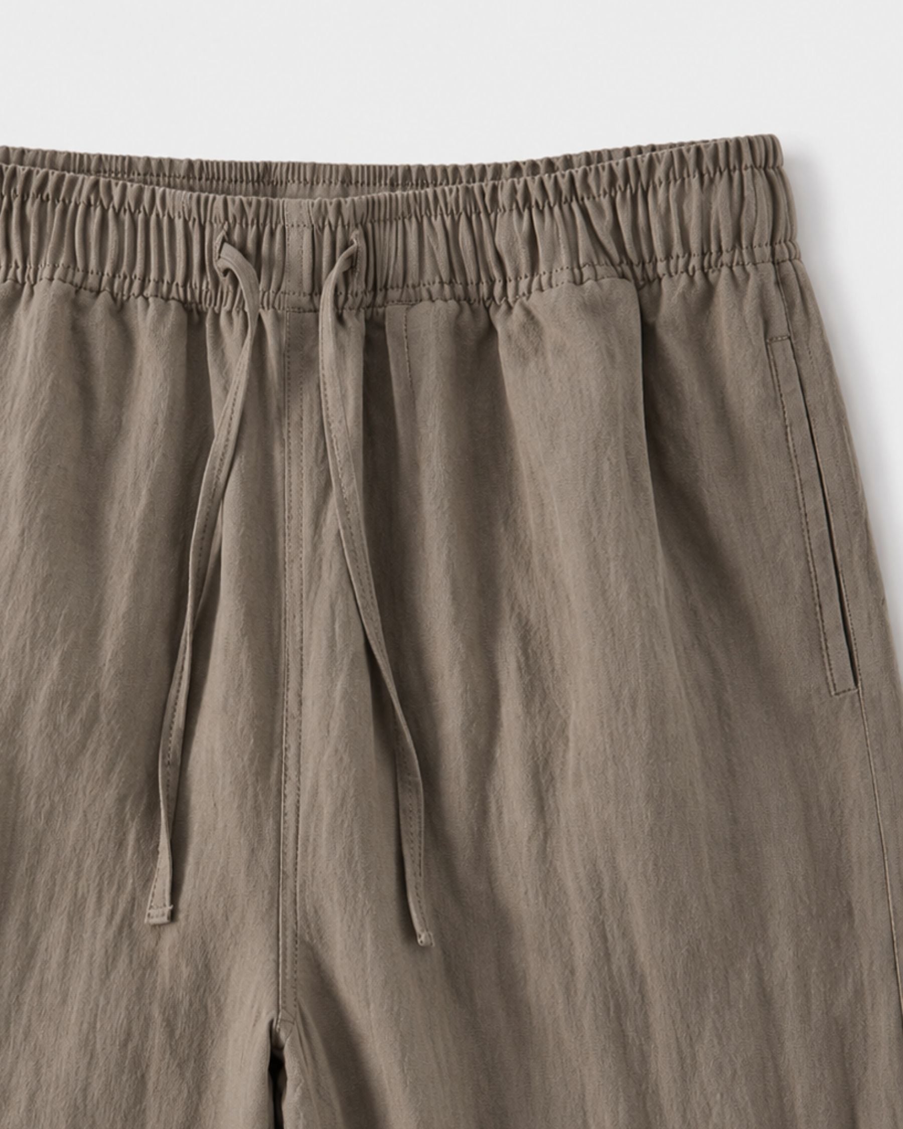 By Alden taupe linen drawstring trousers, close-up detail of elastic waistband and drawstring, light gray background #color_taupe