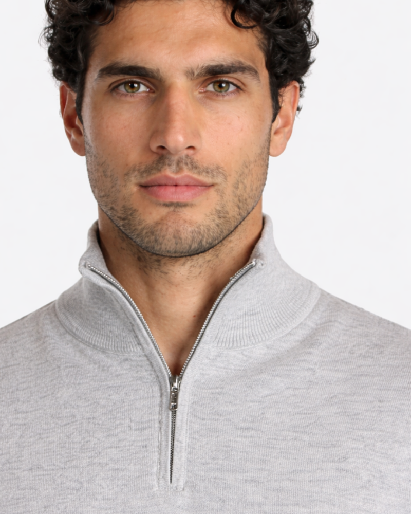 Close-up of a luxury minimalist light grey cotton knit sweater featuring a silver half-zip and ribbed collar detail.