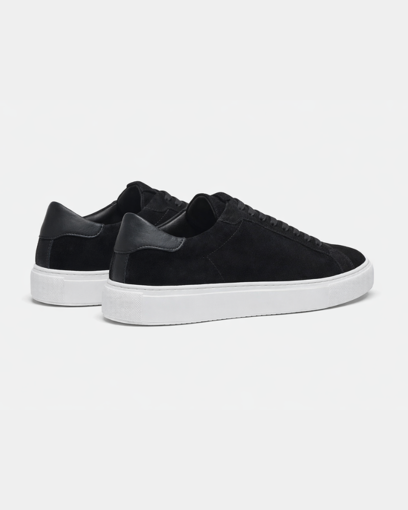 Luxury black suede trainers showcasing the smooth leather heel tab and clean white rubber sole from the back. #color_black