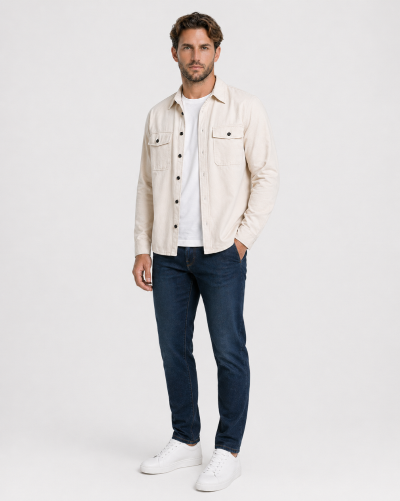 Man wearing a By Alden beige jacket, white shirt, dark jeans, and white sneakers on a light gray background #color_deep stone