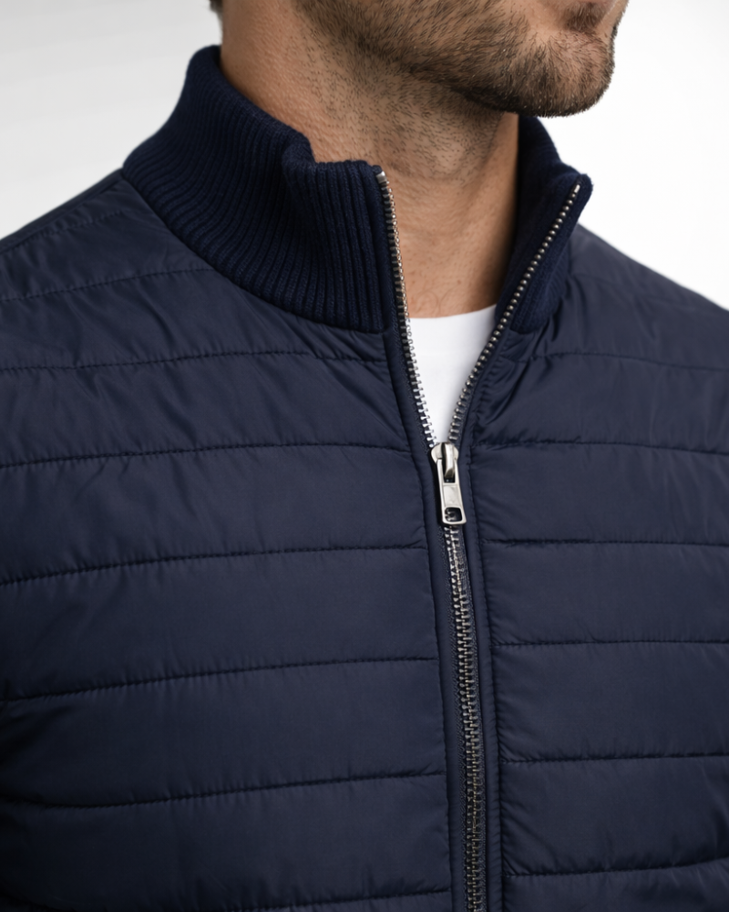 By Alden Navy Hybrid Puffer Knit Jacket worn by a White male model, close-up front view of zip and collar detail, light grey background #Color_Navy
