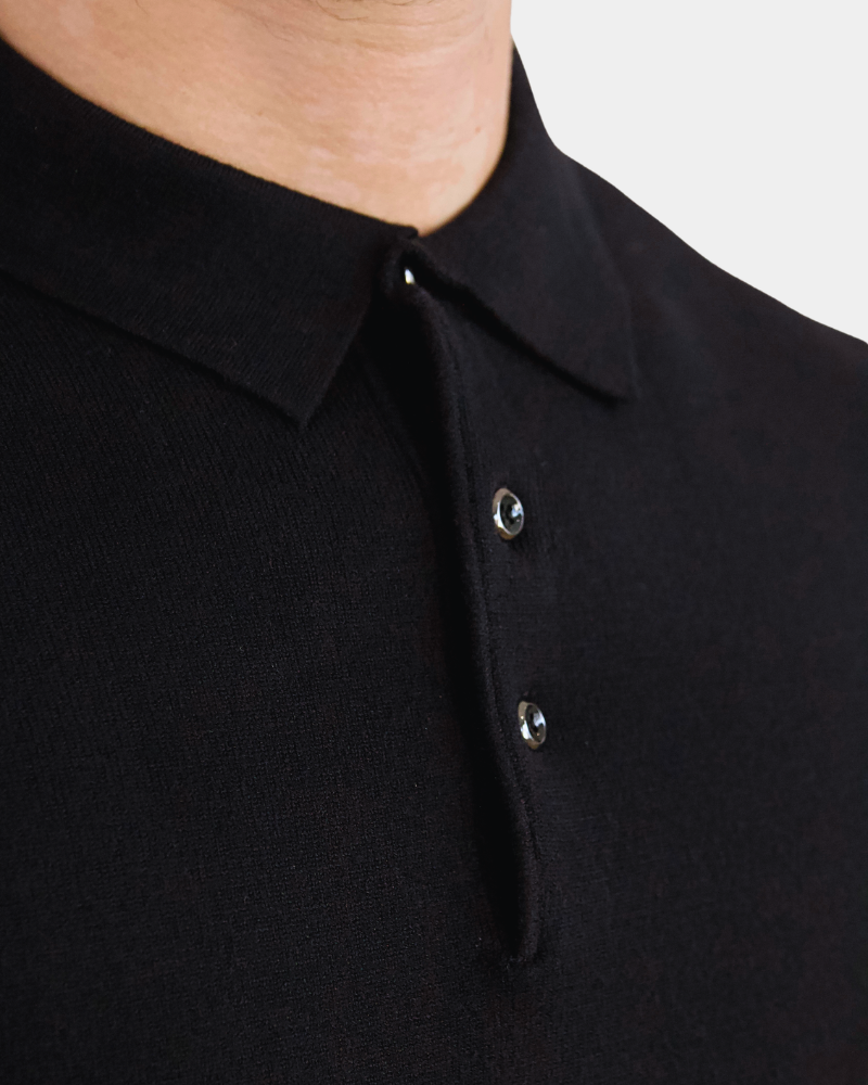 Close-up of luxury black merino wool knit. Minimalist texture with a refined placket and polished button details.
