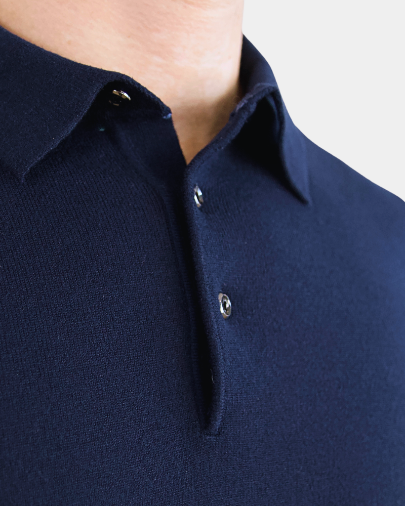 Close-up of luxury navy merino wool knit. Minimalist texture with a precise placket and polished button details.