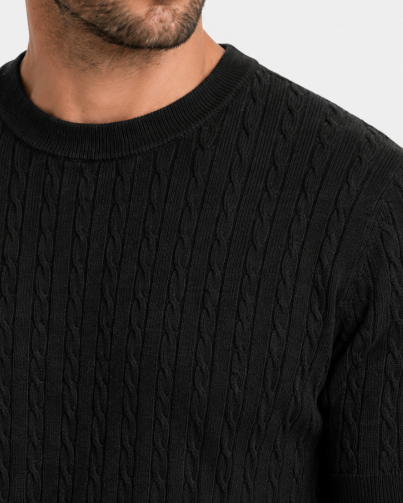By Alden Close-up of a black cable knit sweater on a person against a light gray background #color_black