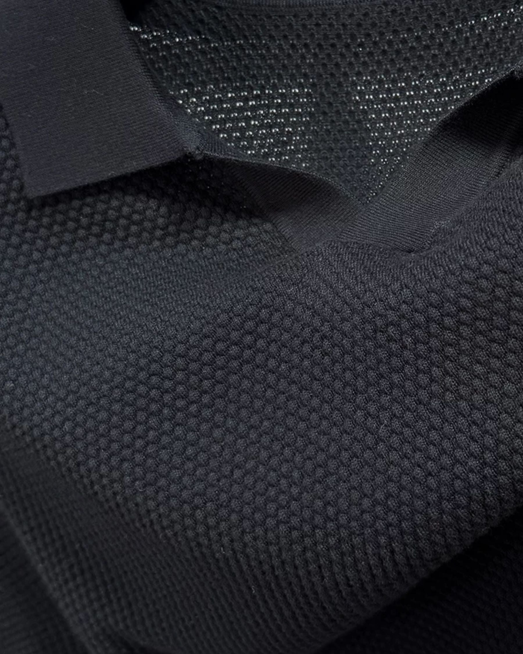 By Alden black open-collar knit polo shirt collar and fabric texture detail, product shot, close-up, black background. #Color_black