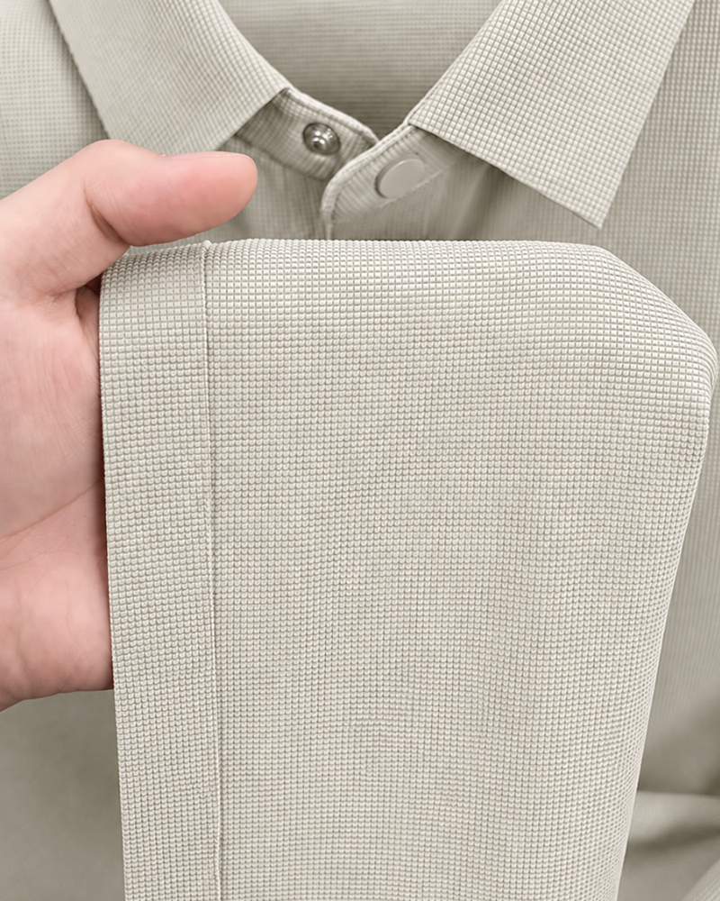 By Alden light gray knit polo shirt fabric texture detail, male model holding hem, extreme close-up, light gray background. #color_deep stone