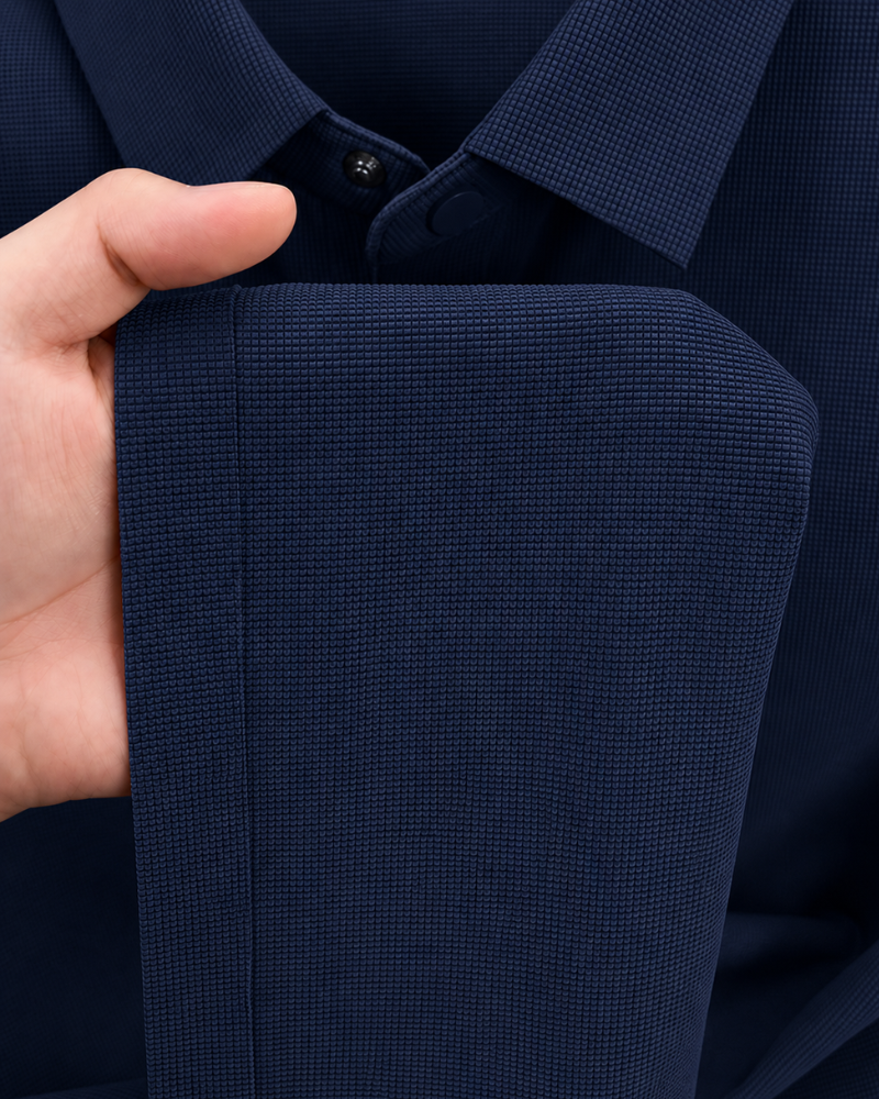By Alden navy blue knit polo shirt fabric texture detail, male model holding hem, extreme close-up, navy background. #color_navy