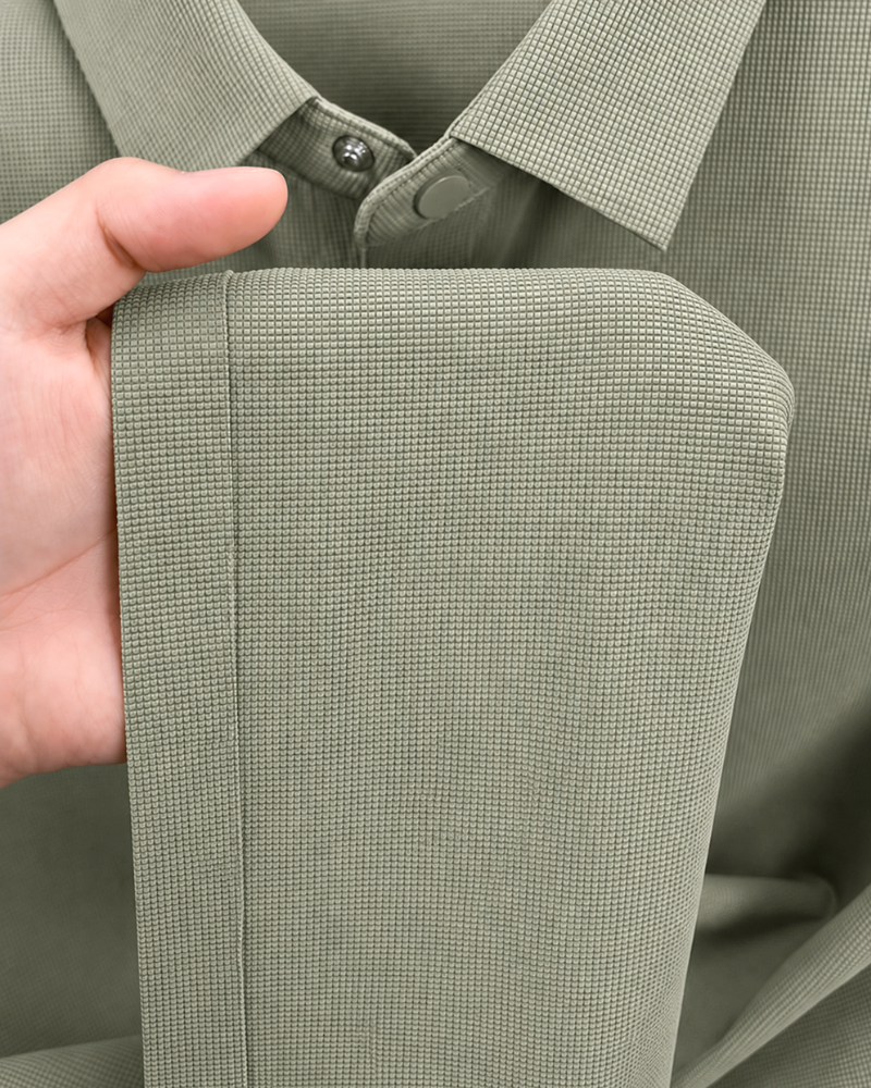 By Alden sage green knit polo shirt fabric texture detail, male model holding hem, extreme close-up, sage background. #color_olive green